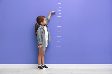 Image of Cute little girl measuring her height near blue wall with scale