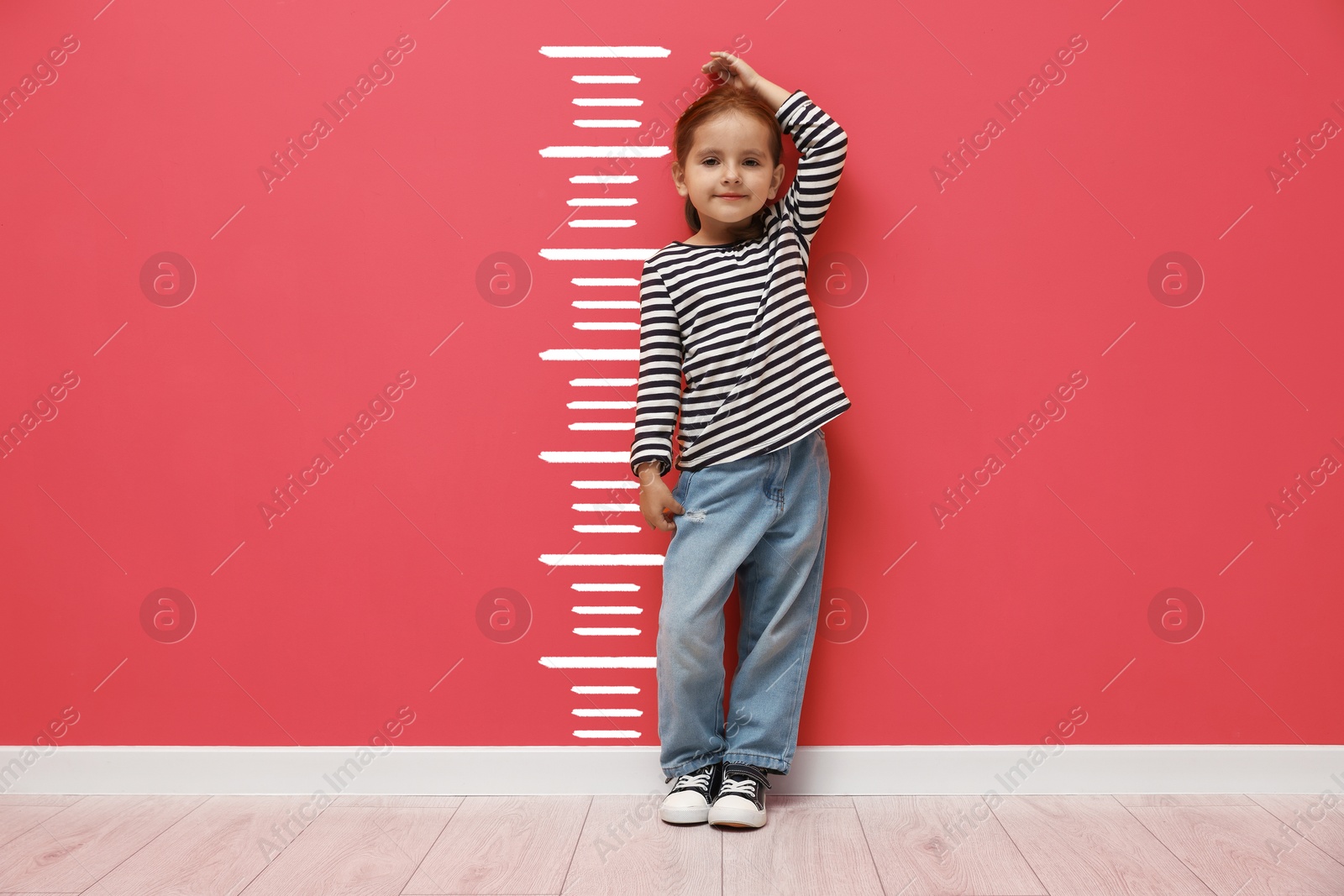 Cute little girl measuring her height near coral color wall with scale Image of Cute little girl measuring her height near coral color wall with scale