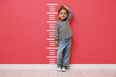 Image of Cute little girl measuring her height near coral color wall with scale