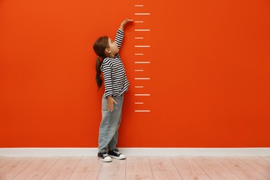 Image of Cute little girl measuring her height near dark orange wall with scale