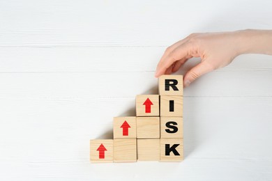 Image of Woman making word Risk of cubes on white wooden background, top view