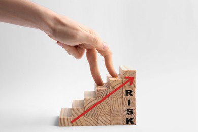 Image of Woman stepping up with fingers on wooden cubes with arrow and word Risk against white background, closeup