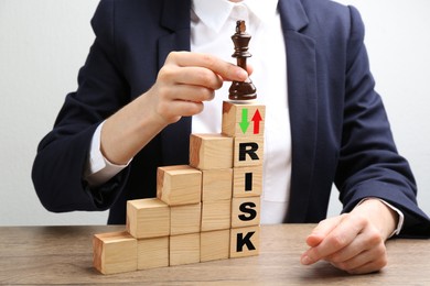 Image of Business woman putting chess king on top of stairs at wooden table, closeup. Cubes with arrows and word Risk