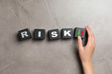 Image of Woman putting cube with arrows next to word Risk on grey table, top view