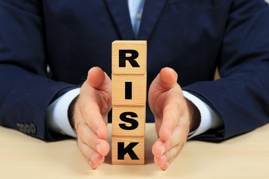 Image of Businessman building word Risk of wooden cubes with letters at table, closeup