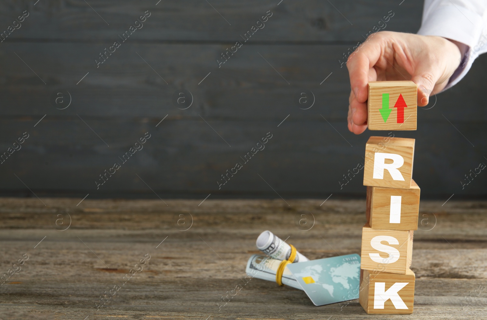 Image of Business risk. Man putting wooden cube with arrows on top of stack, bank card and money on table