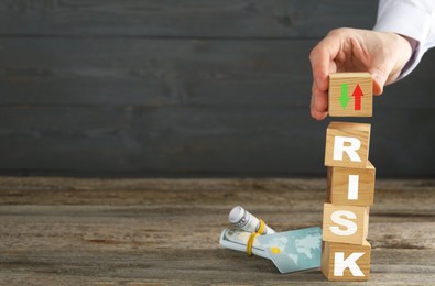 Image of Business risk. Man putting wooden cube with arrows on top of stack, bank card and money on table