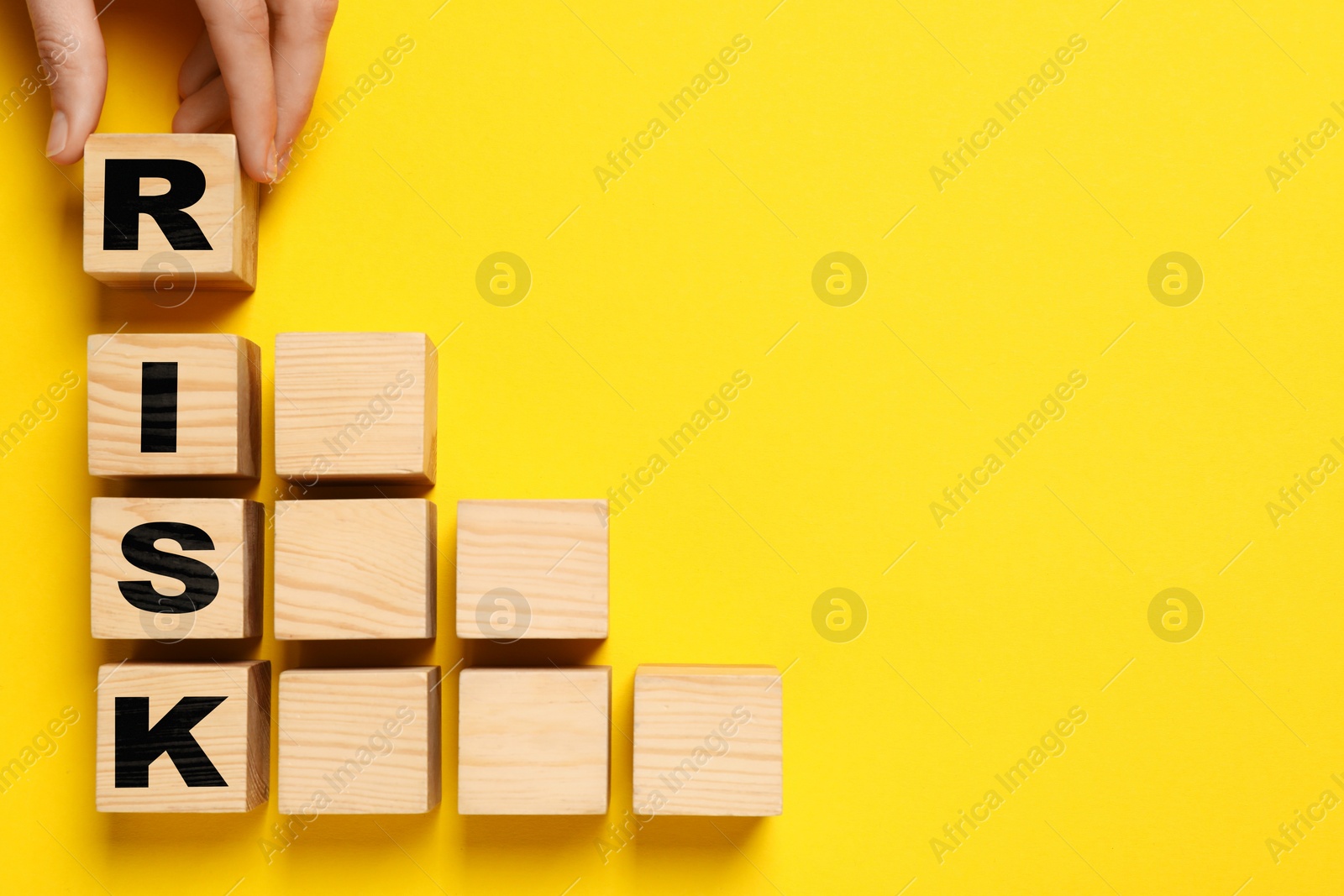 Image of Woman making word Risk with wooden cubes on yellow background, top view