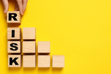 Image of Woman making word Risk with wooden cubes on yellow background, top view