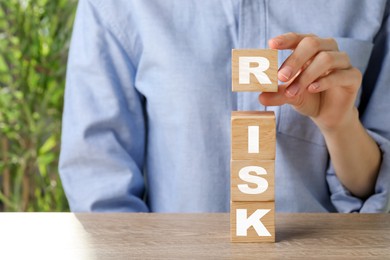 Image of Woman putting wooden cube with letter R to make word Risk at table, closeup