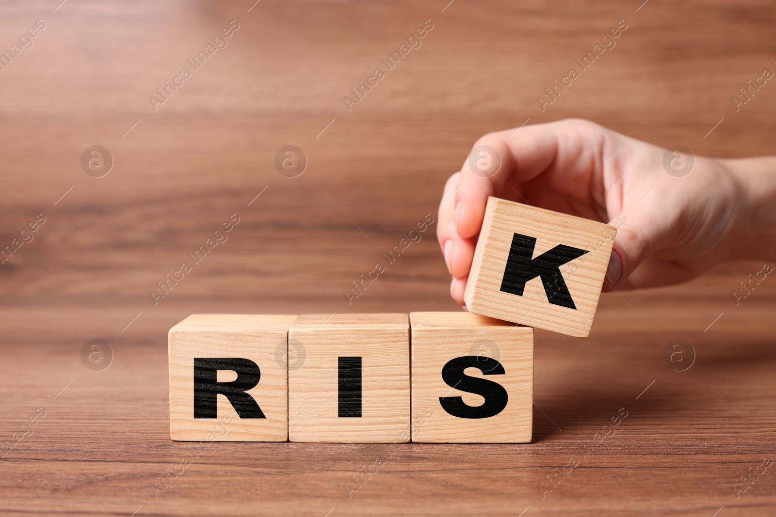 Image of Woman putting wooden cube with letter K to make word Risk at table, closeup