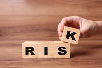 Image of Woman putting wooden cube with letter K to make word Risk at table, closeup
