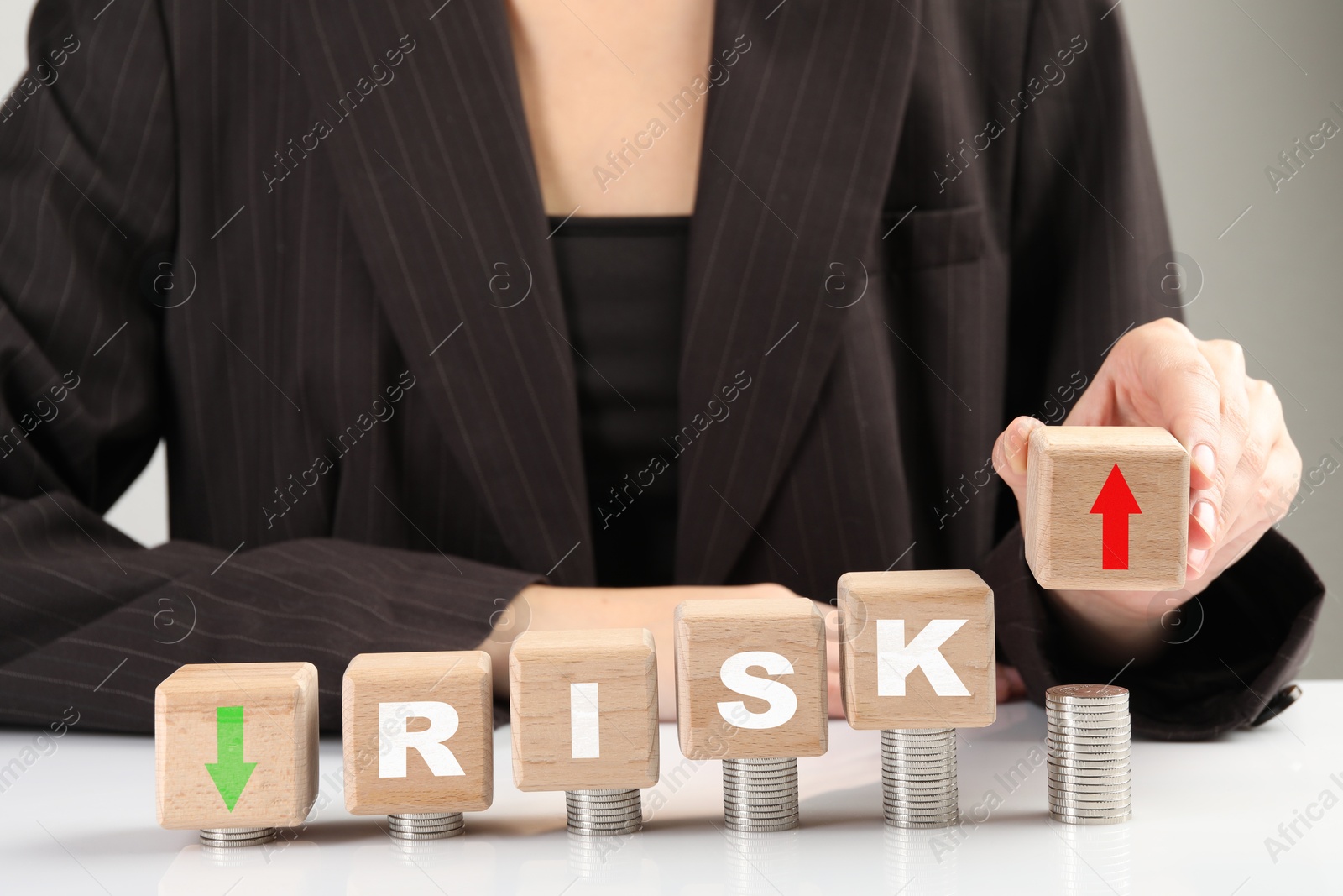 Image of Business risk. Woman putting wooden cube with arrow onto stacked coins at table. closeup