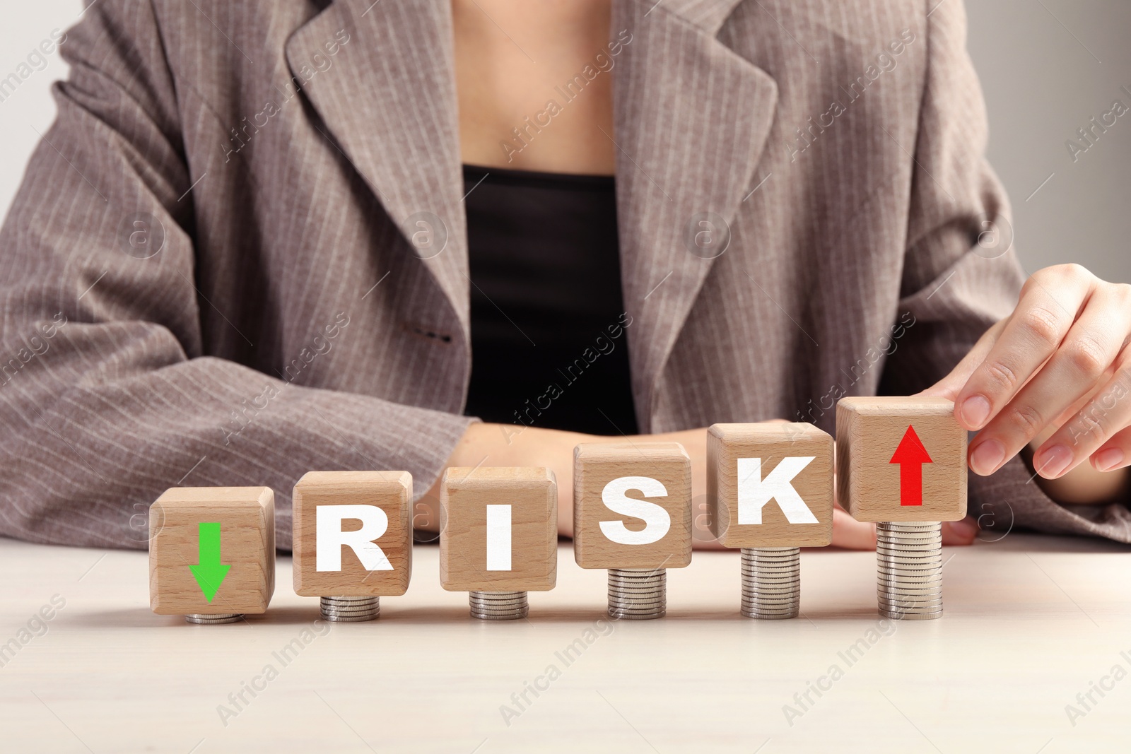 Image of Business risk. Woman putting wooden cube with arrow onto stacked coins at table. closeup