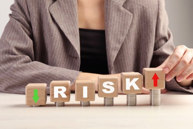 Image of Business risk. Woman putting wooden cube with arrow onto stacked coins at table. closeup