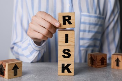 Image of Woman putting wooden cube with letter R to make word Risk at table, closeup