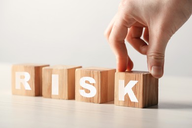 Image of Woman putting wooden cube with letter K to make word Risk at table, closeup