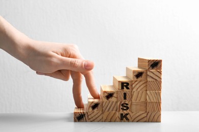 Image of Woman stepping up with fingers on wooden cubes with arrows and word Risk against white background, closeup