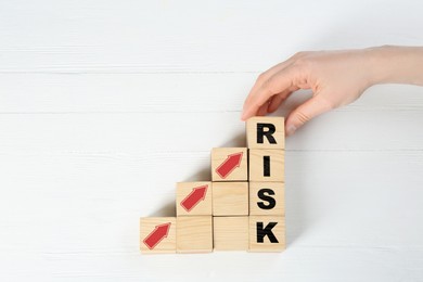 Image of Woman making word Risk of cubes on white wooden background, top view