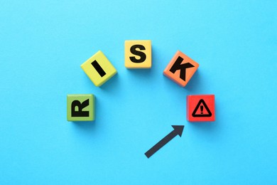Image of Word Risk of wooden cubes with letters on light blue background, top view. Arrow pointing at warning sign