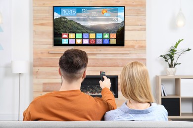 Image of Couple watching TV at home, man using remote control. Menu with icons and information on display