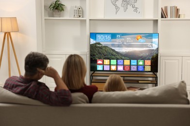 Image of Family watching TV at home, back view. Menu with icons and information on display