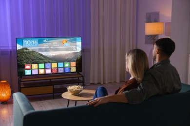 Image of Couple watching TV at home in evening. Menu with icons and information on display