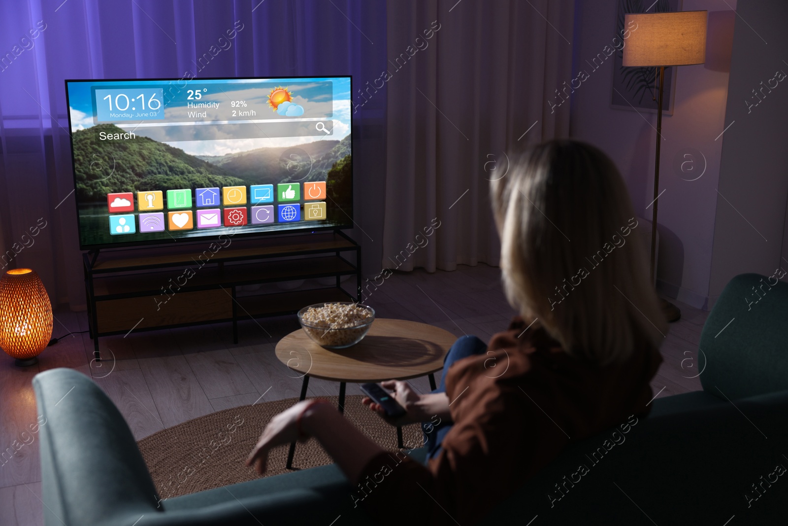 Image of Woman watching TV at home in evening. Menu with icons and information on display