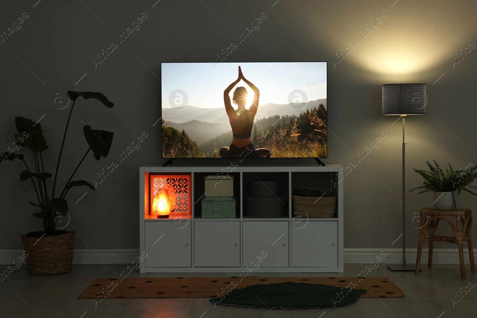 Image of TV set on console in room. Woman meditating in mountains on screen