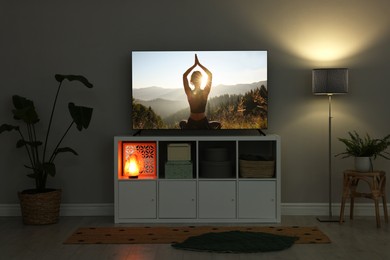 Image of TV set on console in room. Woman meditating in mountains on screen