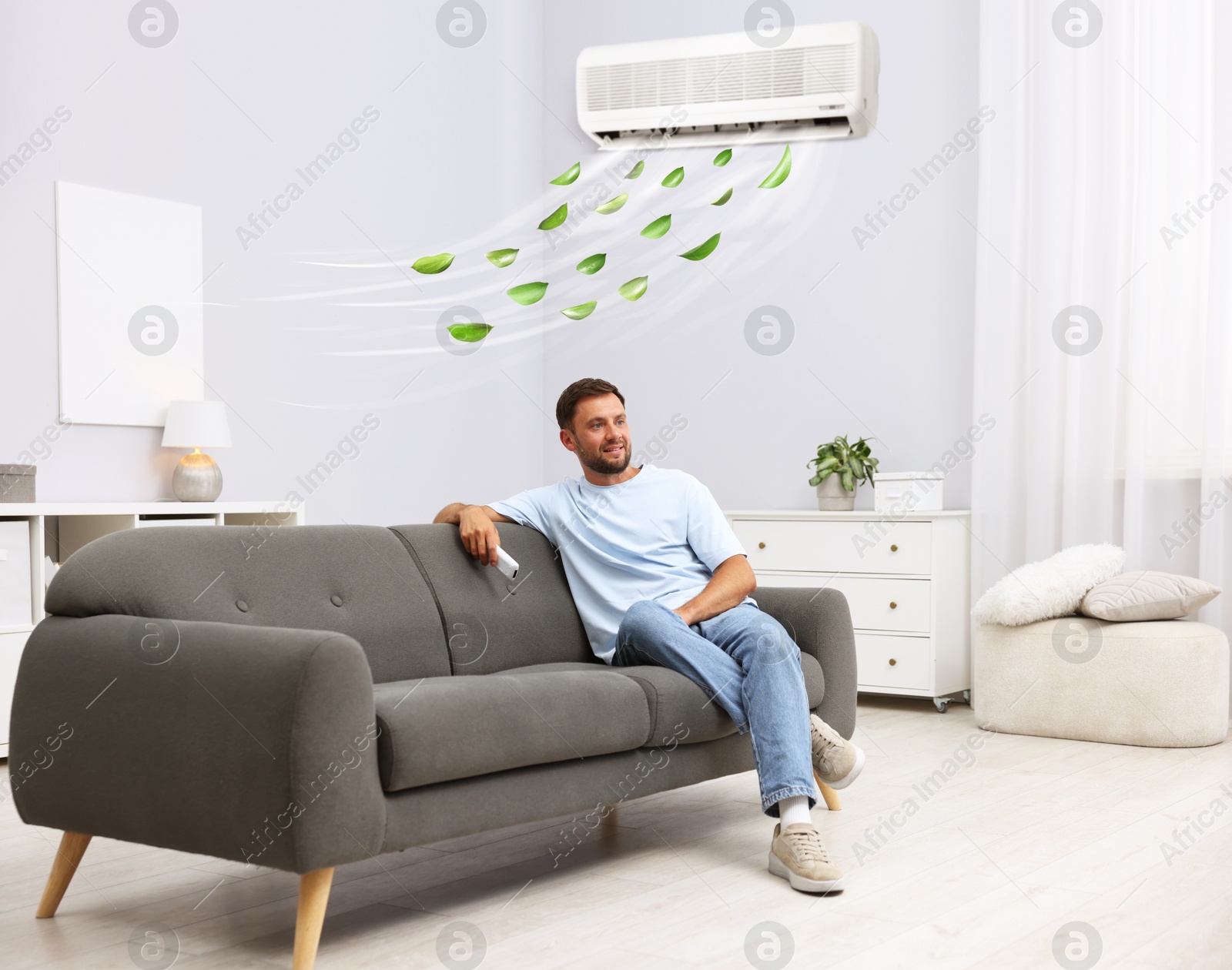Image of Man with air conditioner remote control on sofa at home