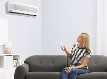 Image of Woman using remote to control air conditioner on sofa at home