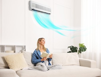 Image of Woman reading book on sofa at home. Air conditioner keeping comfortable temperature indoors