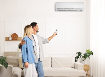 Image of Man using remote to control air conditioner and hugging his girlfriend at home