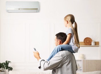 Image of Father and daughter at home. Man using remote to control air conditioner