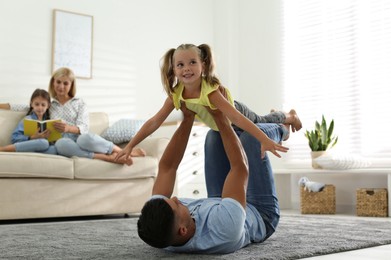 Photo of Happy father playing with his daughter on floor at home