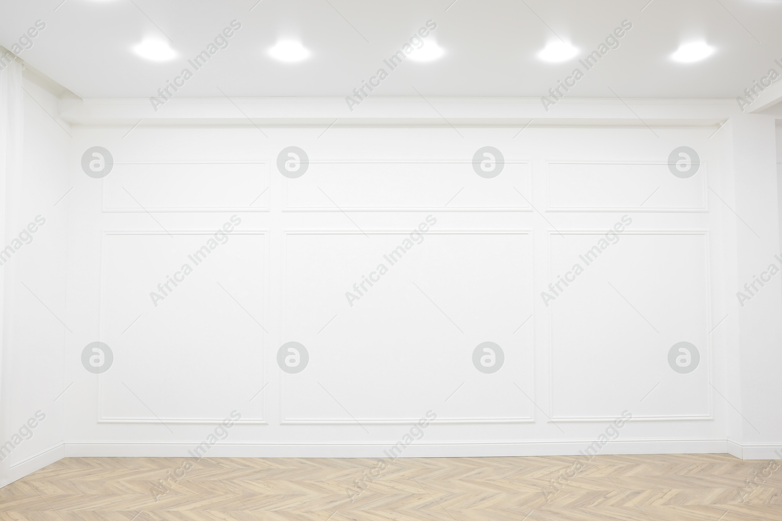 Photo of Empty room with white wall, wooden floor and spot lamps on ceiling