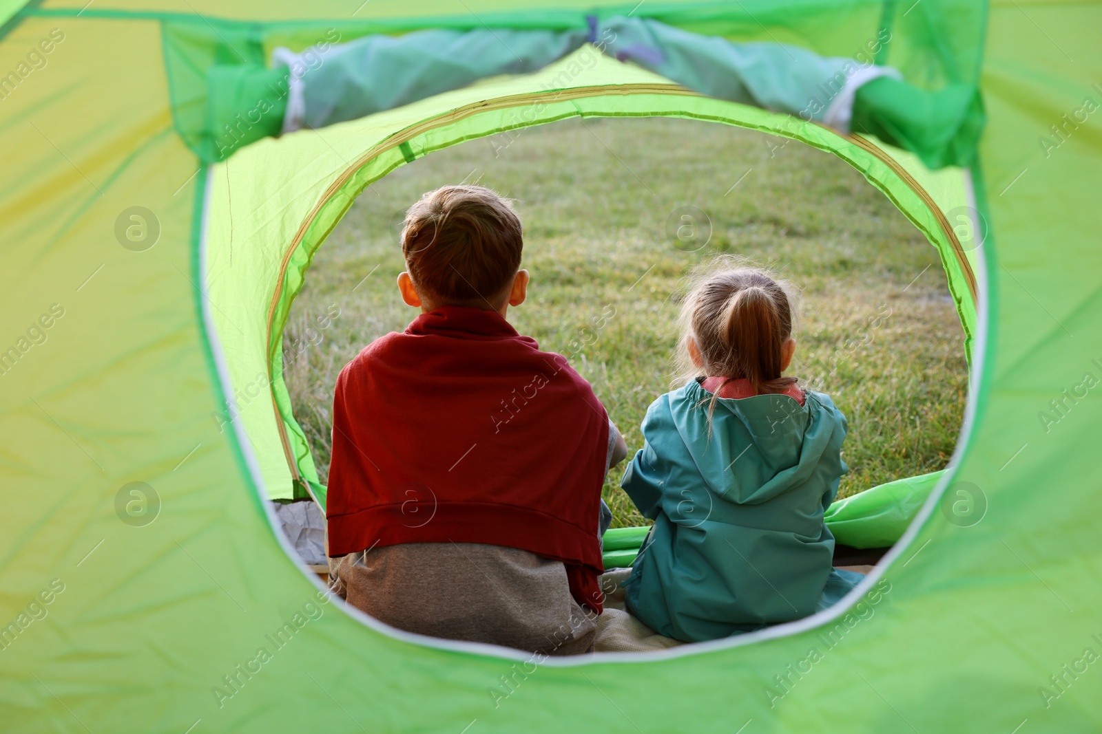 Photo of Brother and sister in camping tent outdoors, back view