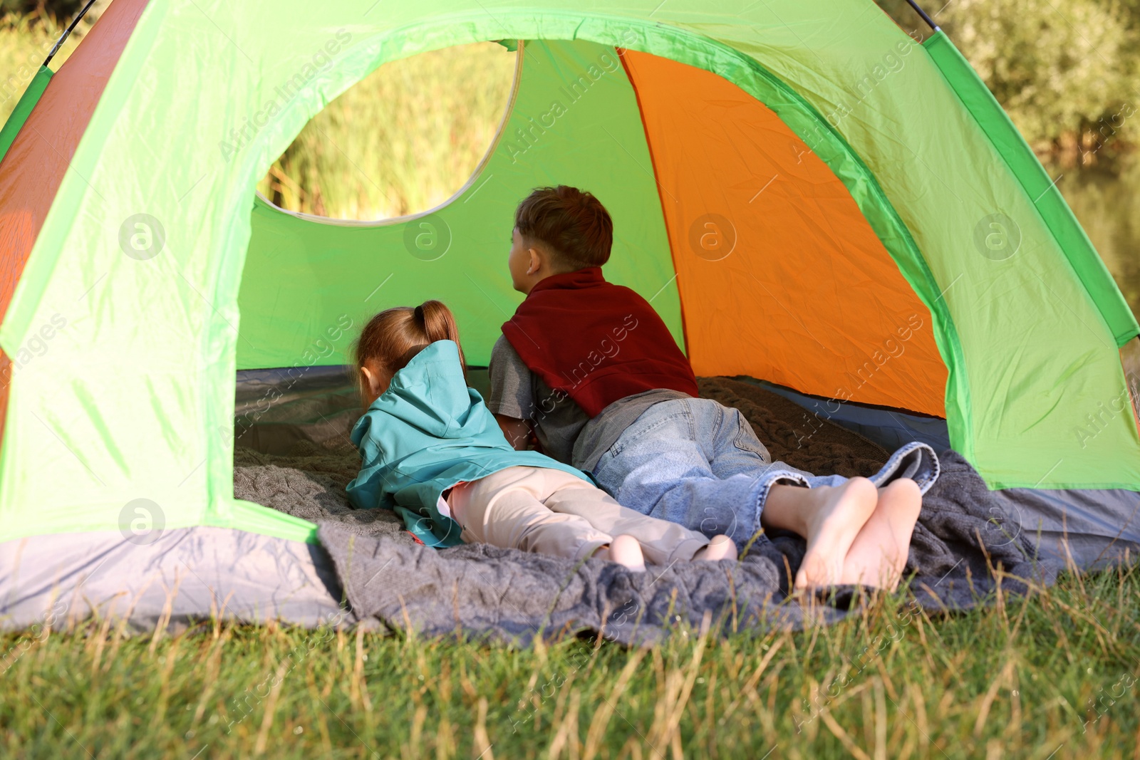 Photo of Brother and sister resting barefoot in camping tent outdoors