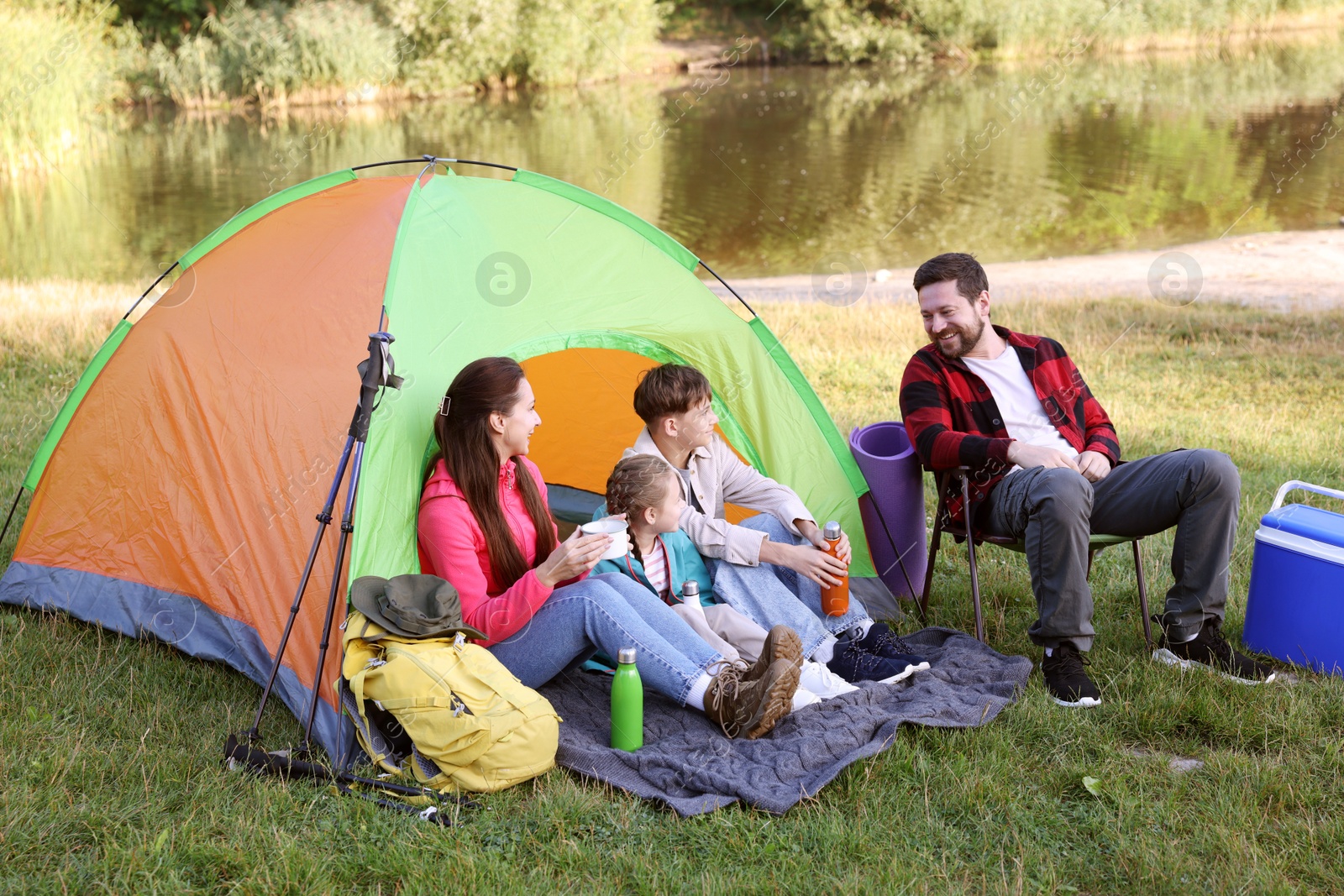 Happy family having break with camping tent, tourist equipment and drinks near river outdoors Photo of Happy family having break with camping tent, tourist equipment and drinks near river outdoors