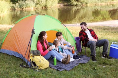 Photo of Happy family having break with camping tent, tourist equipment and drinks near river outdoors