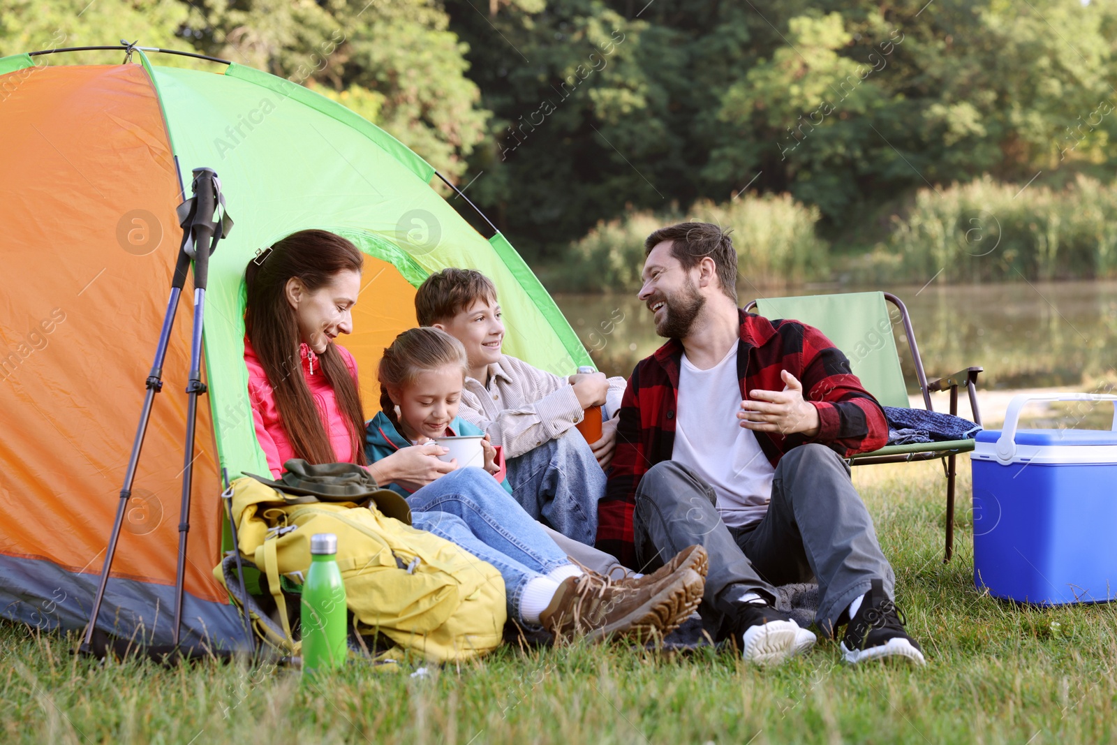 Happy family having break with camping tent, tourist equipment and drinks near river outdoors Photo of Happy family having break with camping tent, tourist equipment and drinks near river outdoors