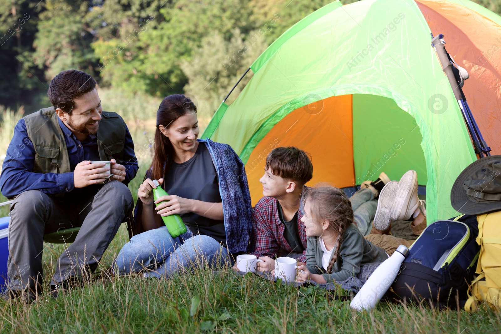 Photo of Happy family spending time together with camping tent and mugs of hot drink outdoors