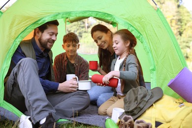 Photo of Happy family spending time together in camping tent with mugs of hot drink outdoors