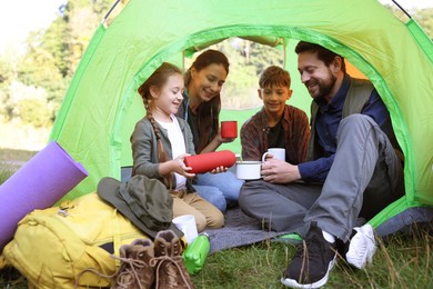 Photo of Happy family spending time together in camping tent with mugs of hot drink outdoors