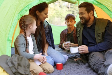 Photo of Happy family spending time together in camping tent with mugs of hot drink outdoors