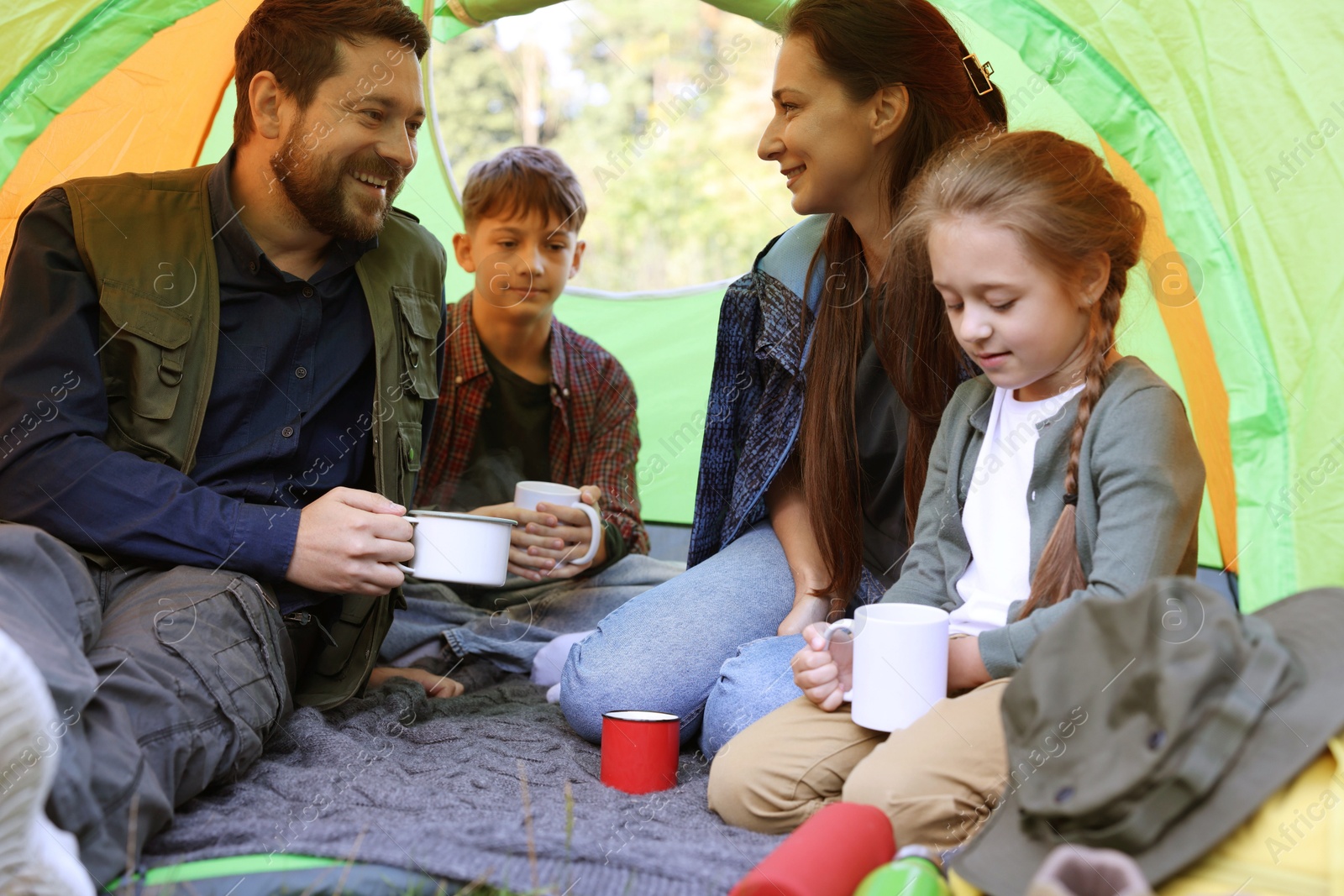Photo of Happy family spending time together in camping tent with mugs of hot drink outdoors