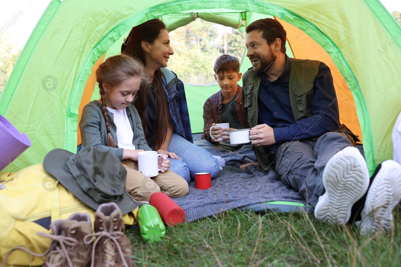 Photo of Happy family spending time together in camping tent with mugs of hot drink outdoors