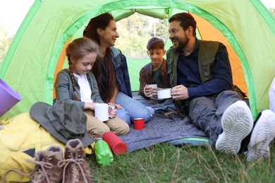 Photo of Happy family spending time together in camping tent with mugs of hot drink outdoors