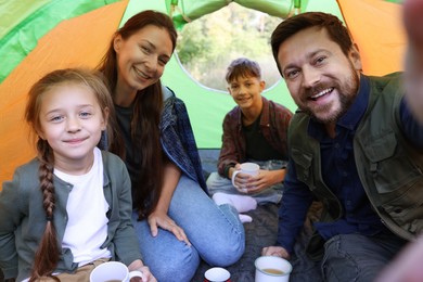 Photo of Happy family taking selfie in camping tent with mugs of hot drink outdoors